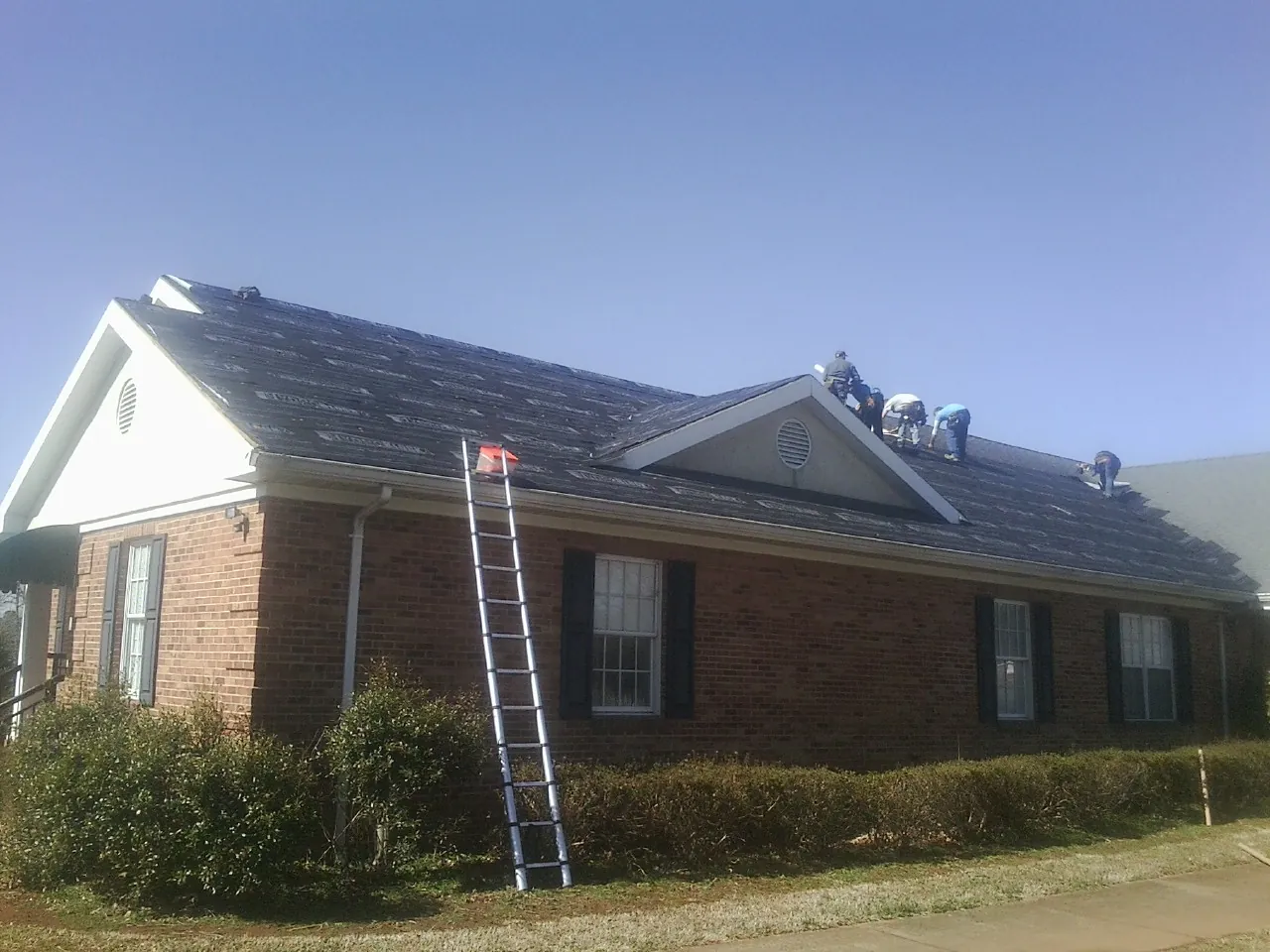 Crew tearing shingles off a brick ranch roof with a ladder set — Emergency Roof Repair work by our crew in Flintstone