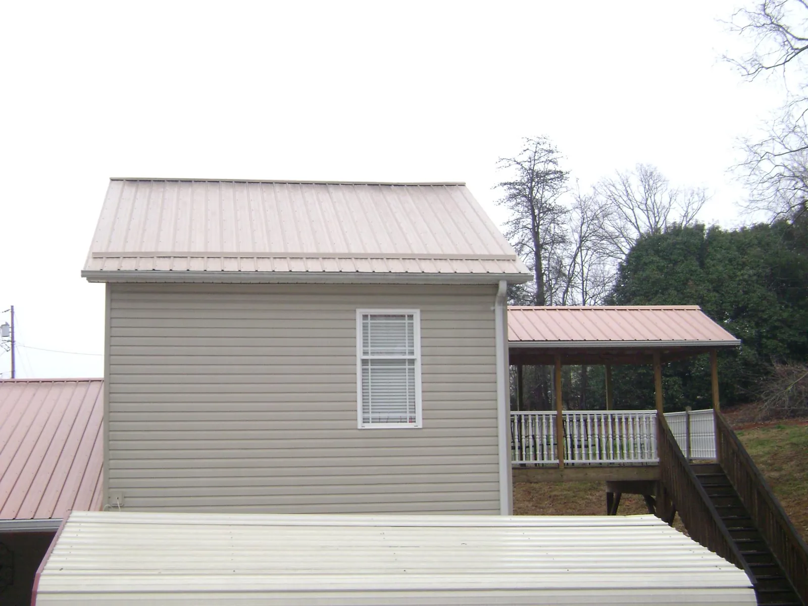 Tan metal roofs on a two story addition and attached porch, from a Roof Replacement job in Flintstone